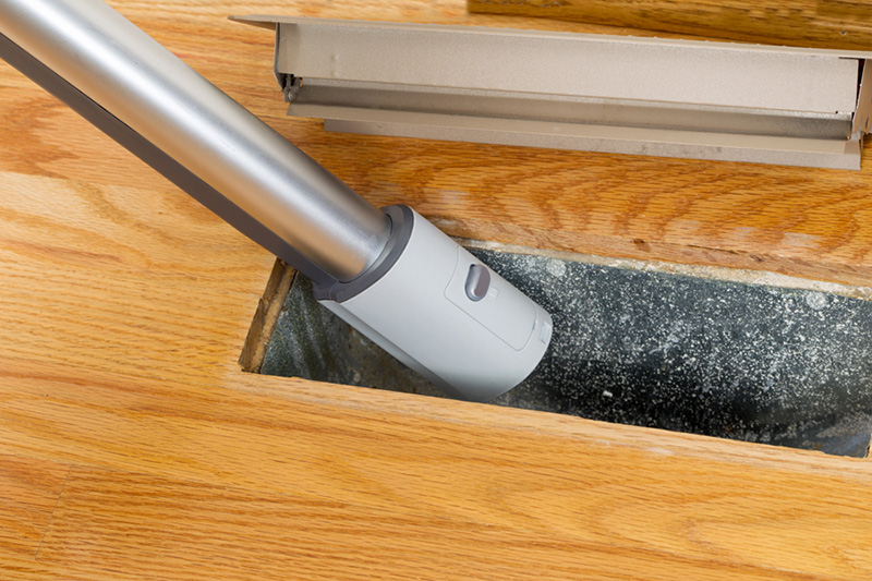 Vacuum suctioning dust out of floor register. 7 Furnace Maintenance Tips.