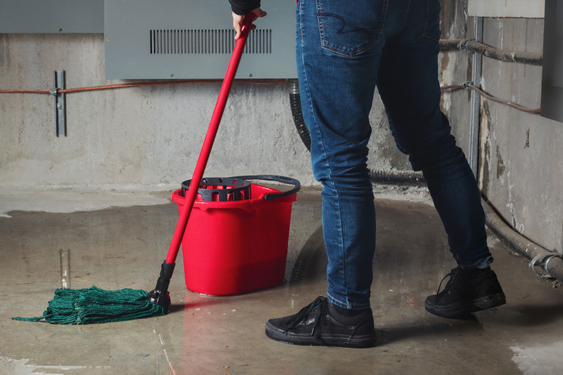 technician mopping up water on basement floor.