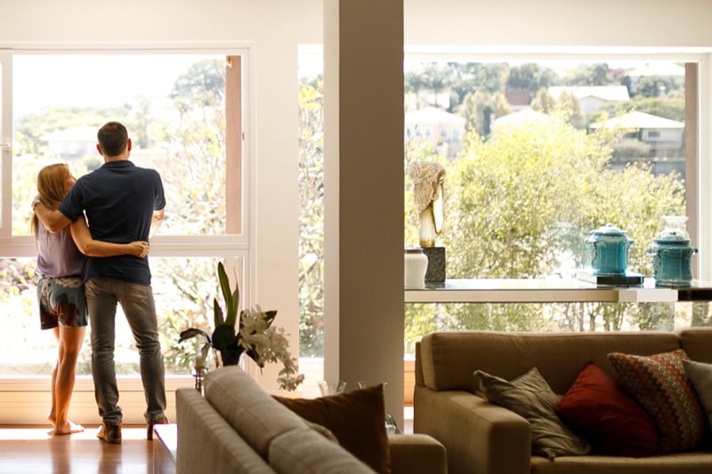 3 Tips to Prevent AC Breakdown During a Heat Wave. Photo of a couple looking out a large window from their living room.