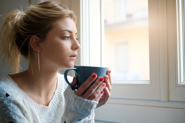 A woman sits in front of a window with a cup. Why Isn’t My Furnace Heating My Entire Home?